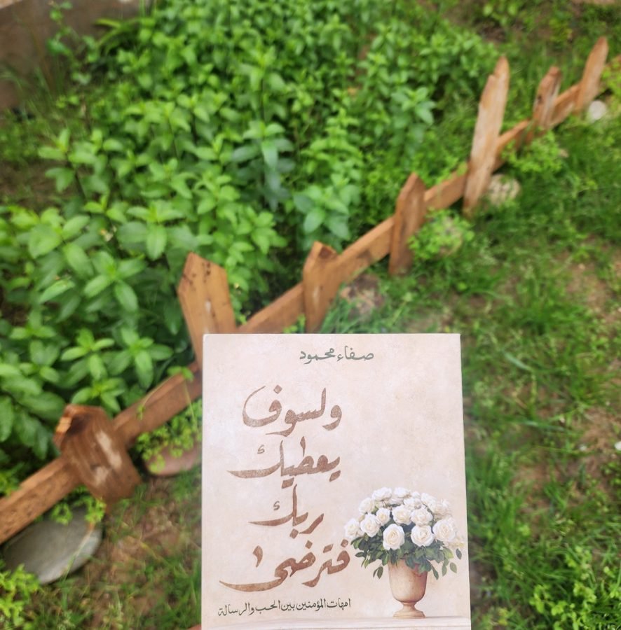 نسخة مطبوعة من الكتاب في حديقة بين نباتات خضراء وسياج خشبي.